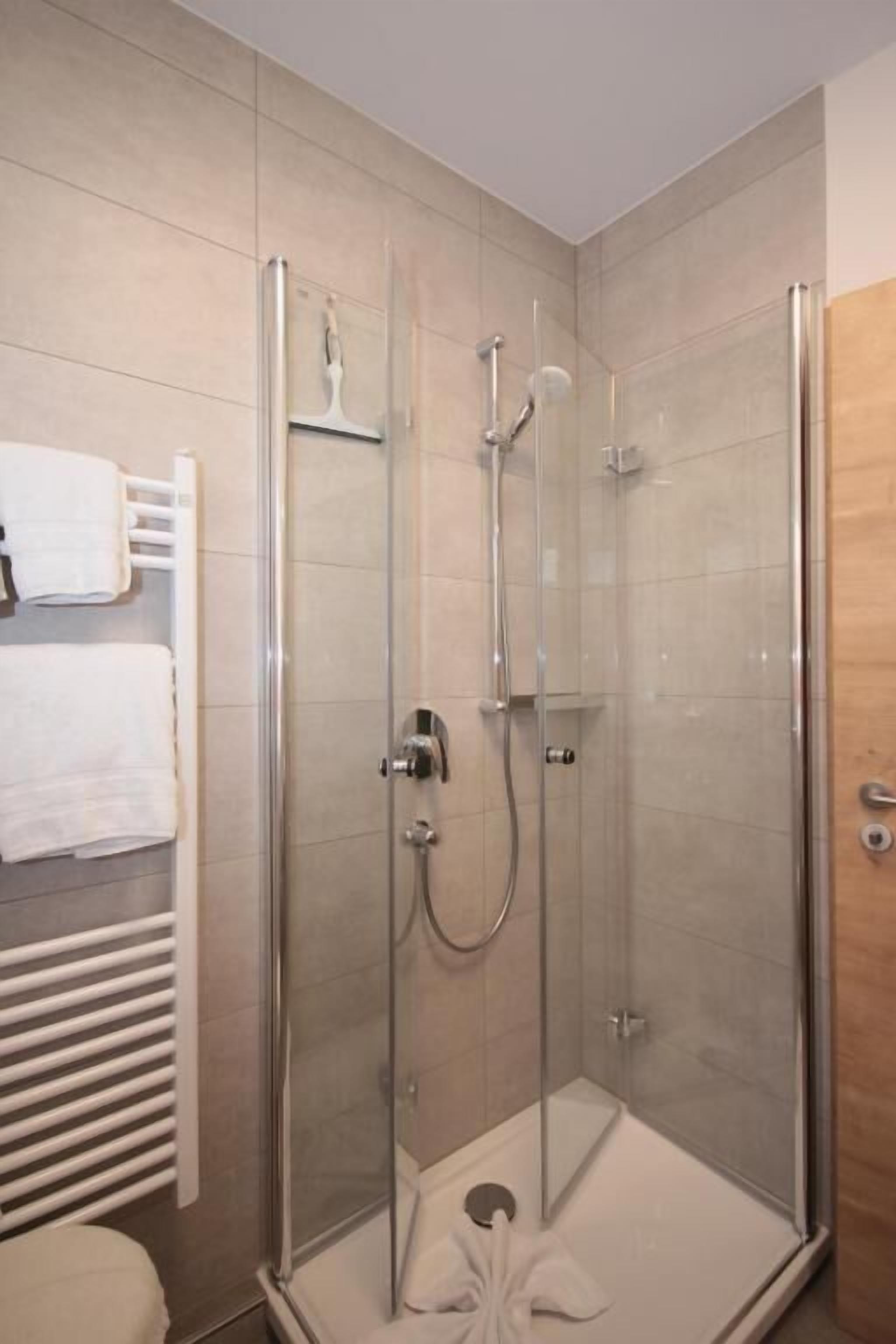 Eine begehbare Duschkabine mit Handbrause, einem Händetuchhalter an der Wand und einem weißen Handtuch auf dem Boden.