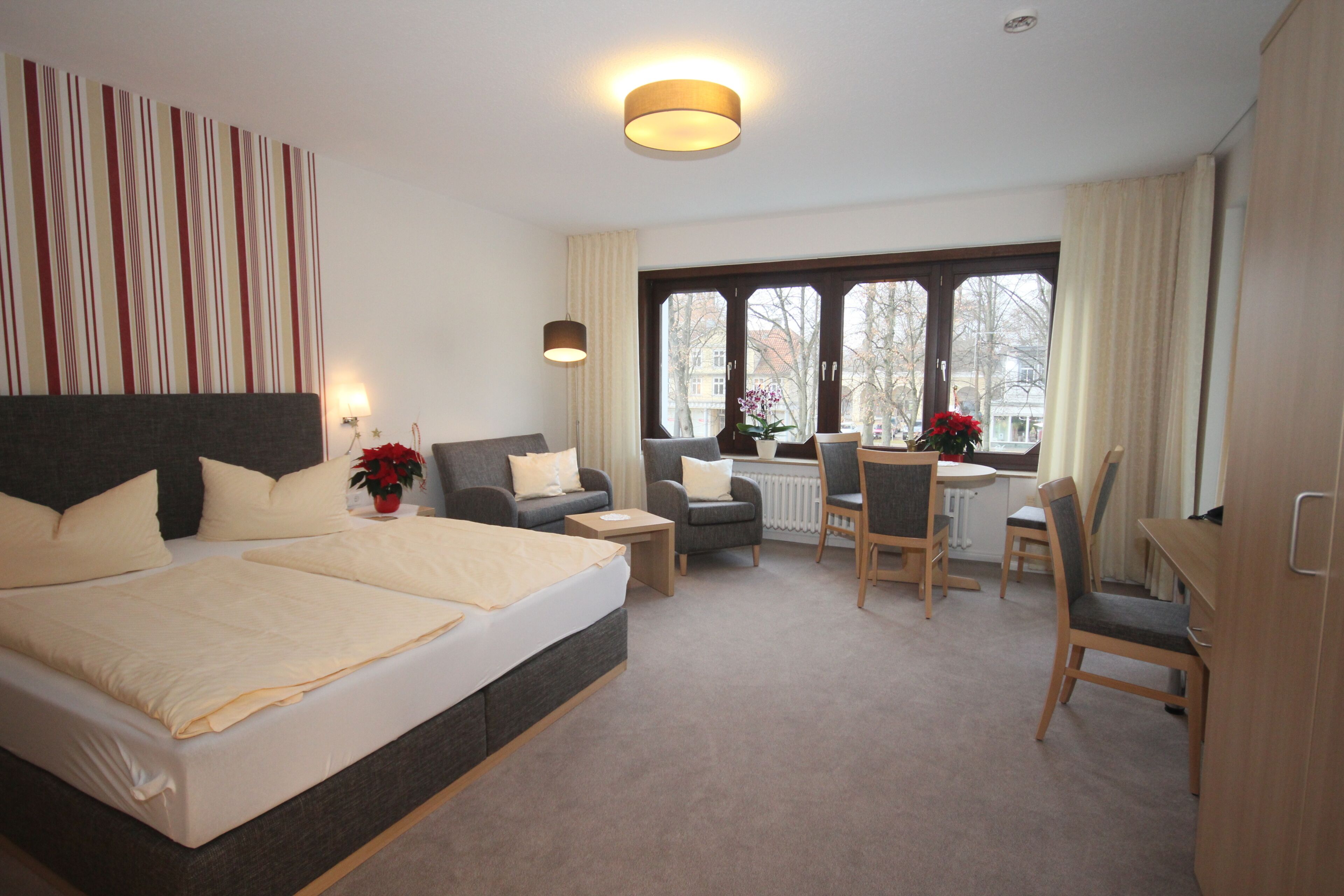 Hotelkamer met een groot bed, een bank, een eettafel met stoelen, een raam met gordijnen en een radiator.