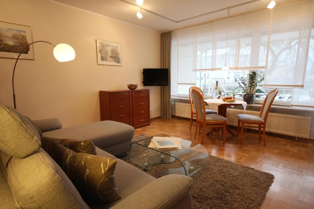 Una sala de estar con un sofá, una mesa de centro de vidrio, un televisor y un comedor con sillas y una mesa.