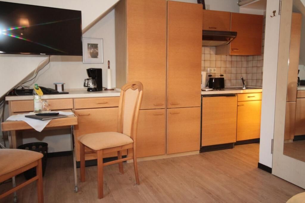 Une cuisine compacte avec des meubles en bois, un coin repas avec une chaise et un téléviseur fixé au-dessus du comptoir.