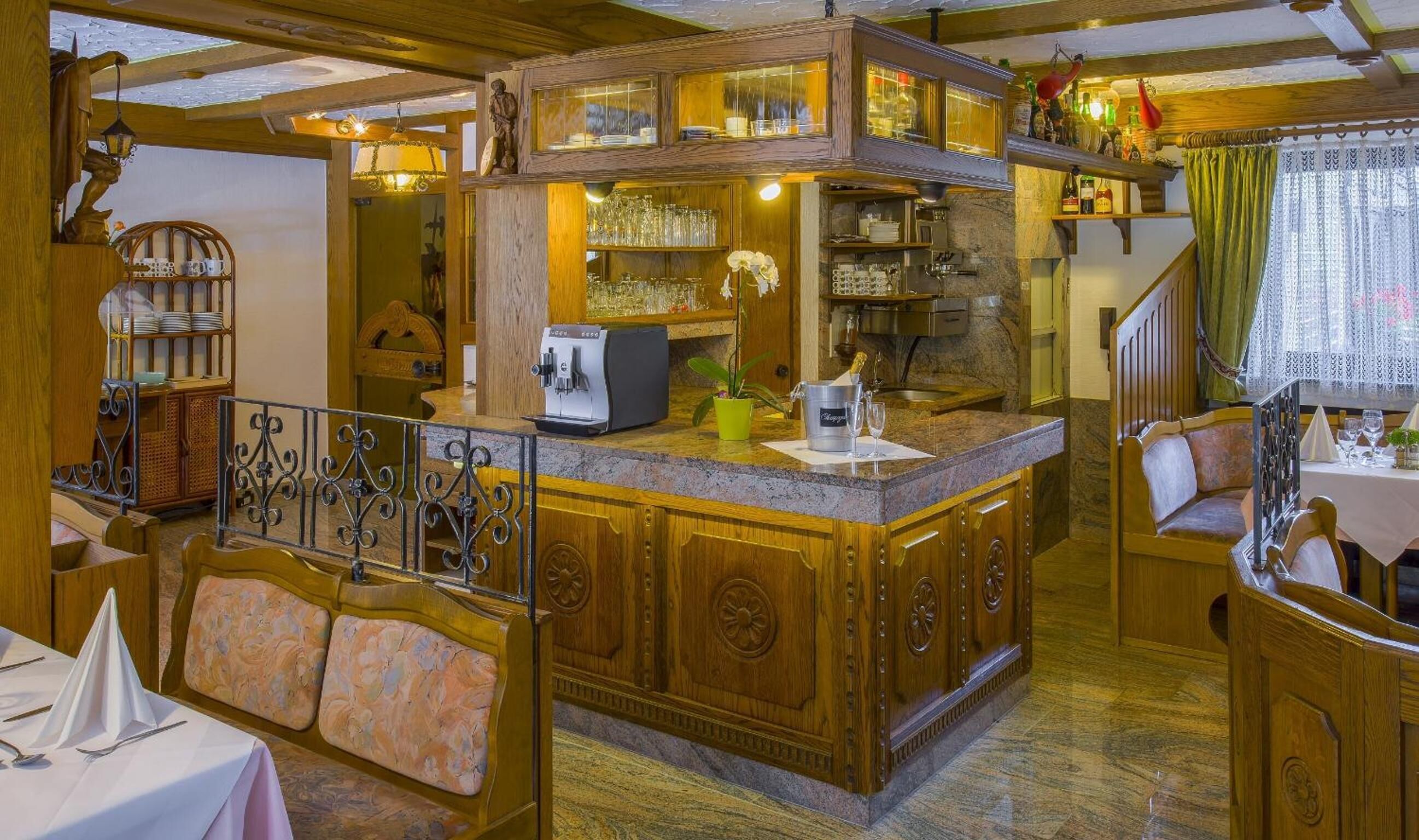 A cozy restaurant with a wooden bar, seating area, and a staircase.