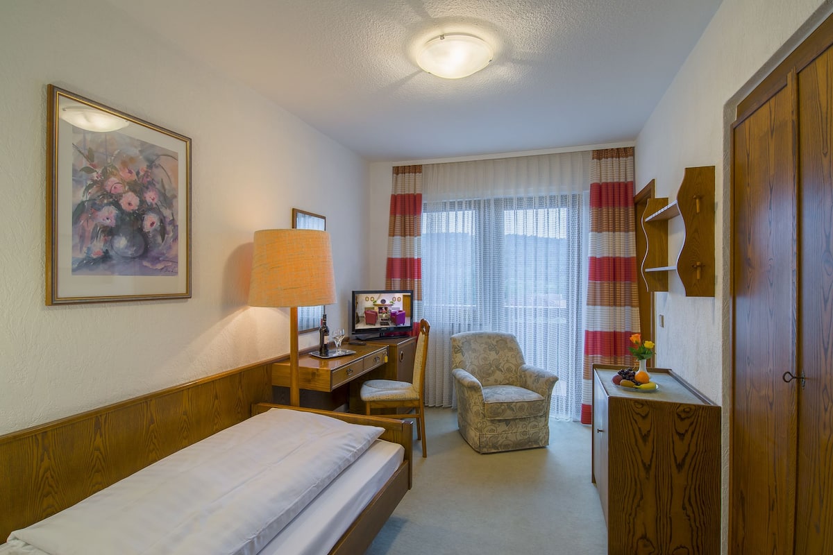 Ein Hotelzimmer mit einem Bett, einem Schreibtisch mit Computer, einem Stuhl und einem Holzschrank.