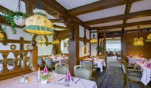 Un restaurante con vigas de madera, candelabros colgantes y mesas dispuestas para comer.