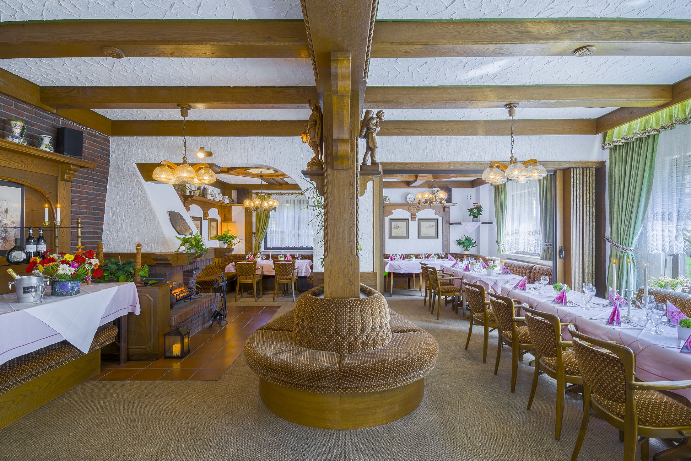 A spacious dining area with high wooden beams, a central seating area, and multiple dining tables set for guests.