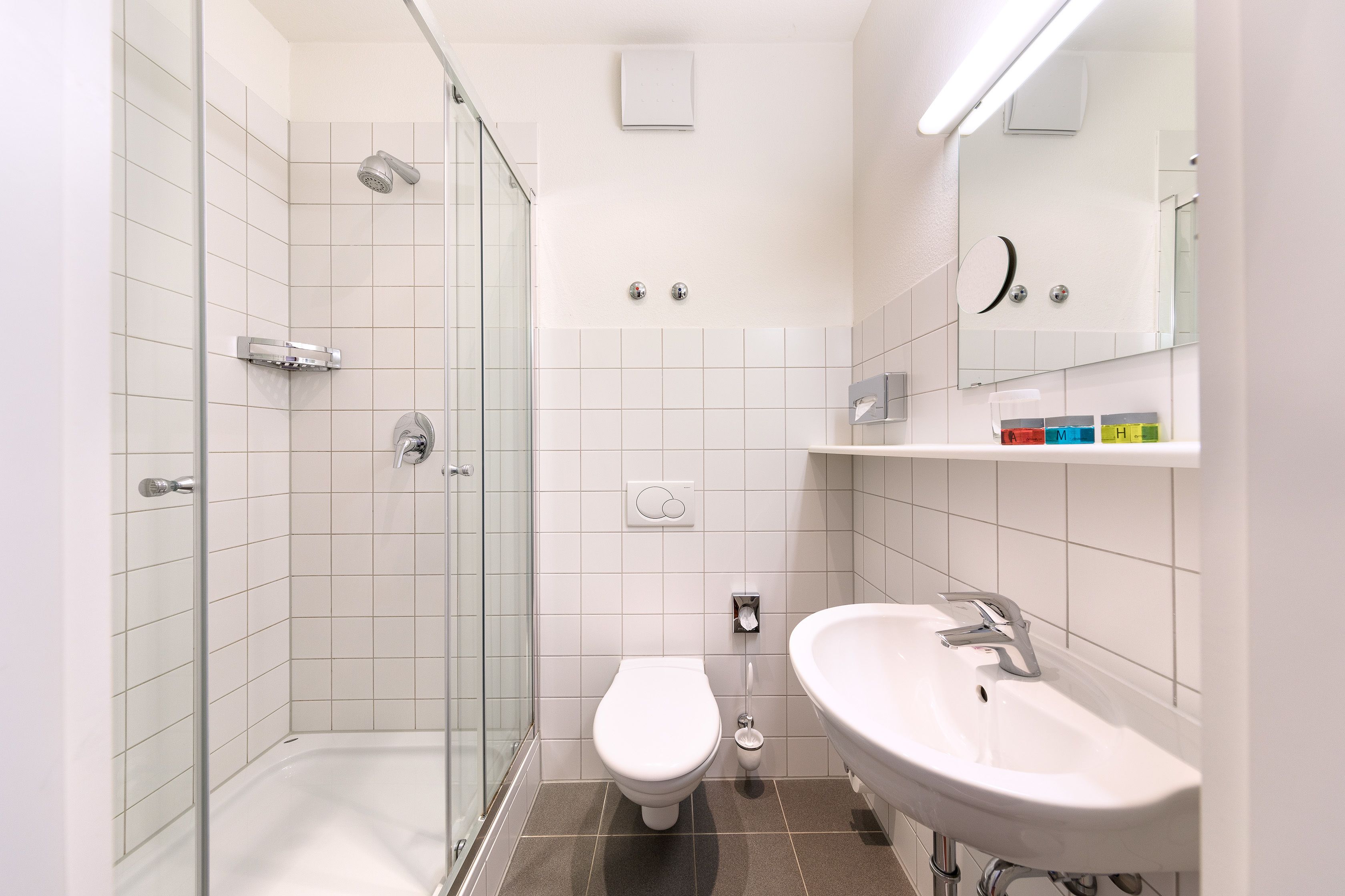 Ein modernes Badezimmer mit Duschkabine aus Glas, einer weißen Toilette und einem Waschbecken mit Spiegel darüber.