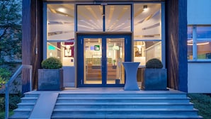 A modern building entrance with a glass door, a staircase, and two potted plants. - AMH Airport-Messe-Hotel (Filderstadt)
