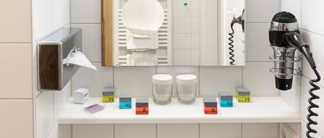 Un baño con lavamanos blanco, secador de pelo y espejo. Hay bloques de colores con letras sobre el lavamanos.