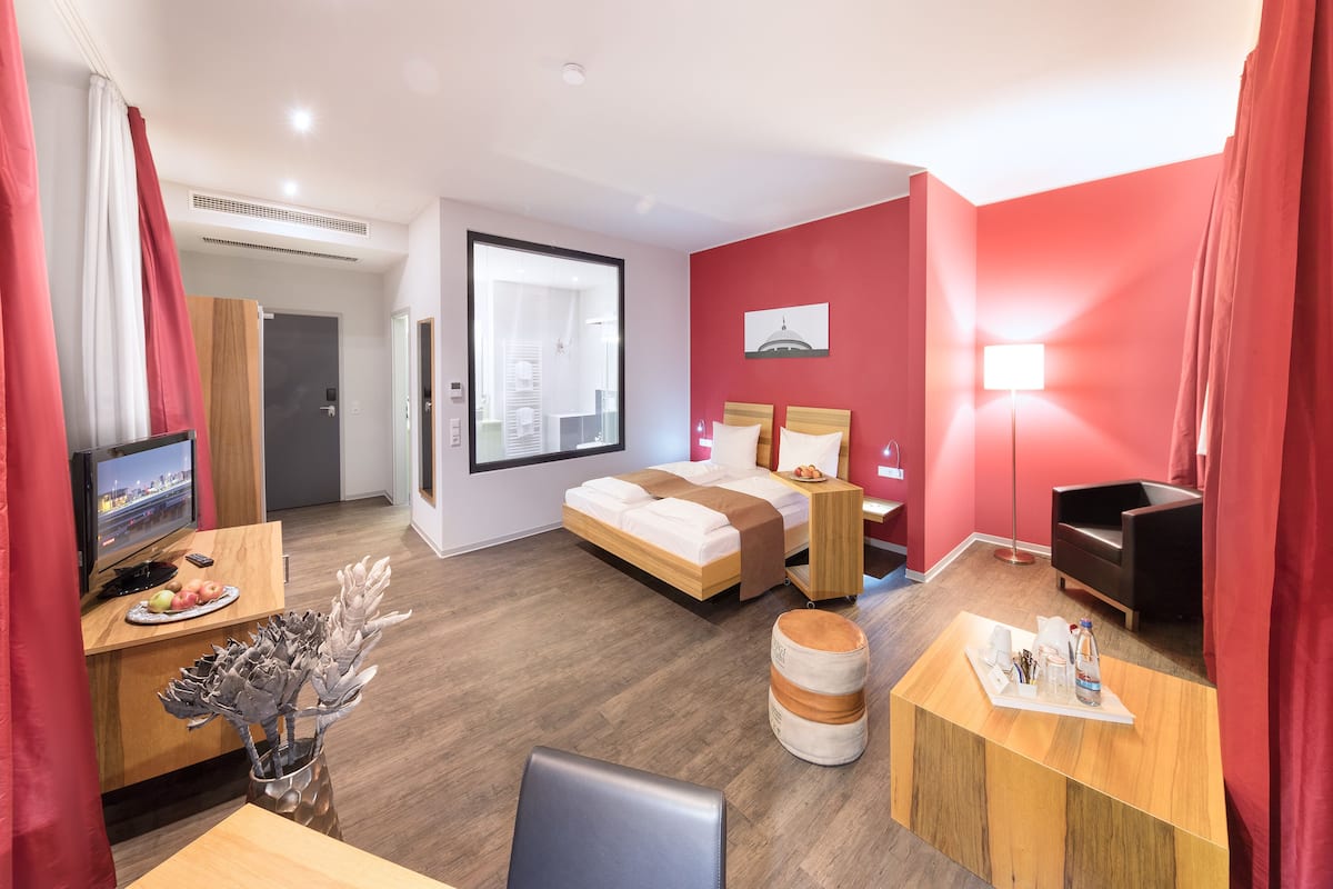A modern hotel room with a bed, desk, TV, and a city view.
