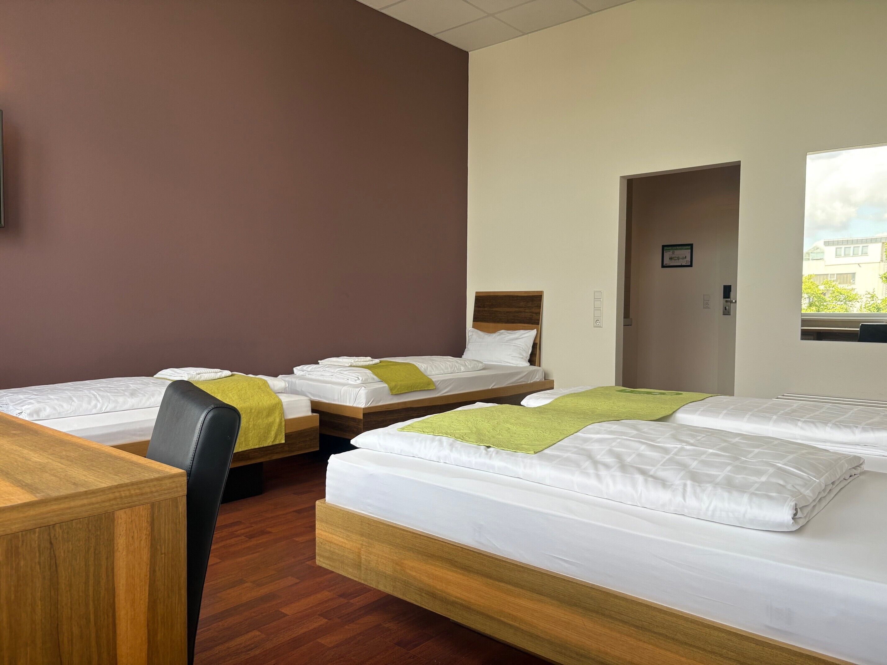 A hotel room with three beds, wooden headboards, and a desk.