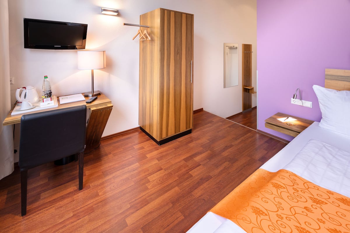 A hotel room with a wooden desk, a television, a bed with an orange blanket, and a purple wall.