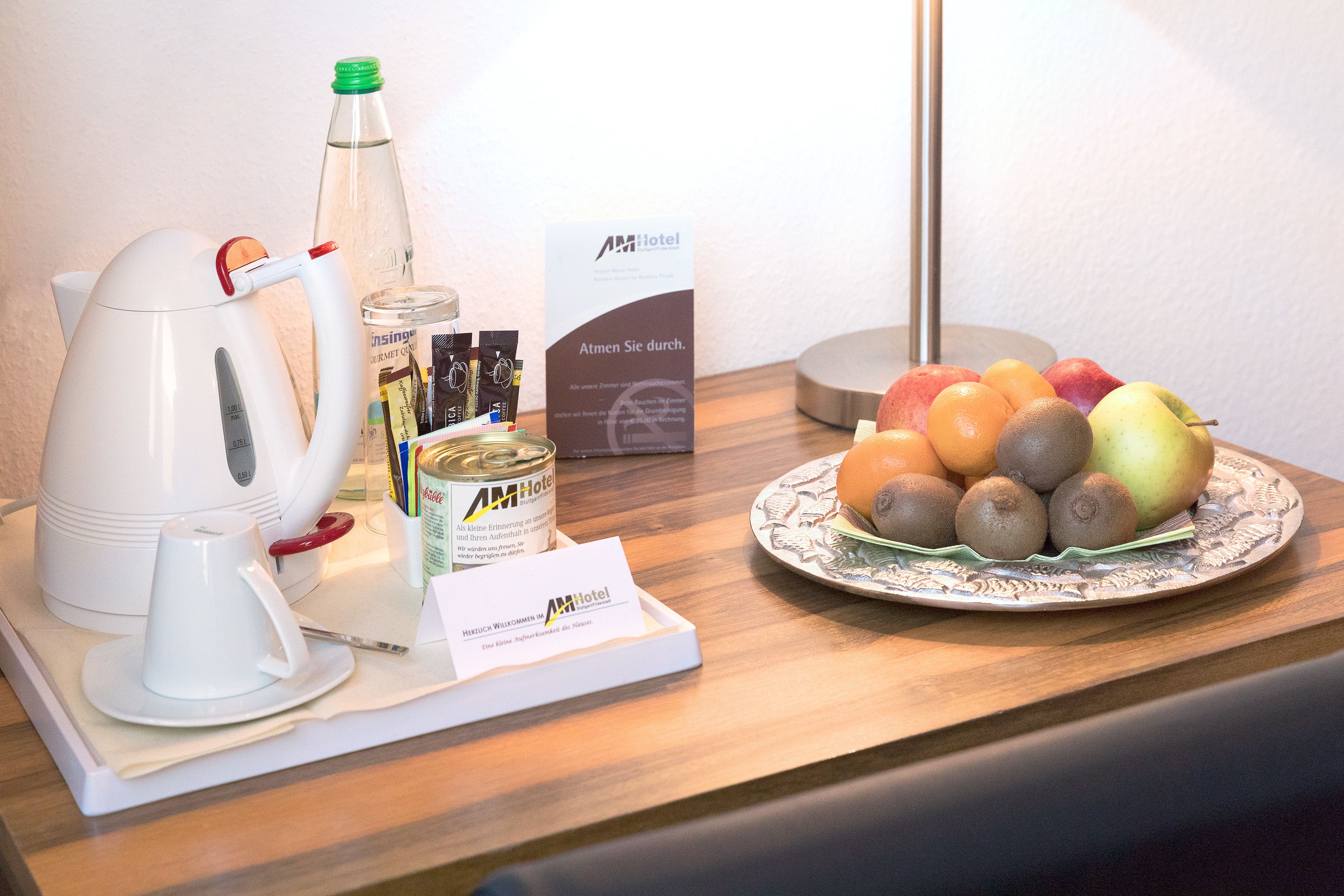 A table with a kettle, a bottle, a plate of fruit, and a welcome card.