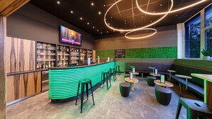 A modern bar area with a green-lit counter, multiple stools, and a television screen. - AMH Airport-Messe-Hotel (Filderstadt)