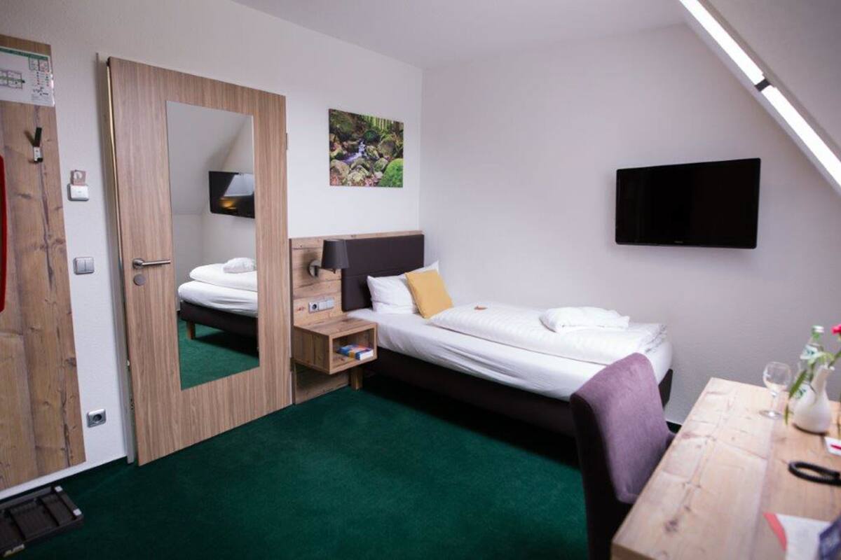 Een kleine hotelkamer met een bed, nachtkastje, spiegel en een televisie aan de muur.