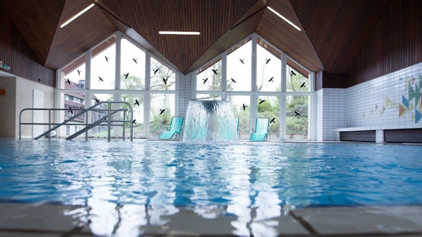An indoor swimming pool with a waterfall feature, large windows, and a tiled floor. - BSW - Erlebnishotel Festenburg (Clausthal-Zellerfeld)