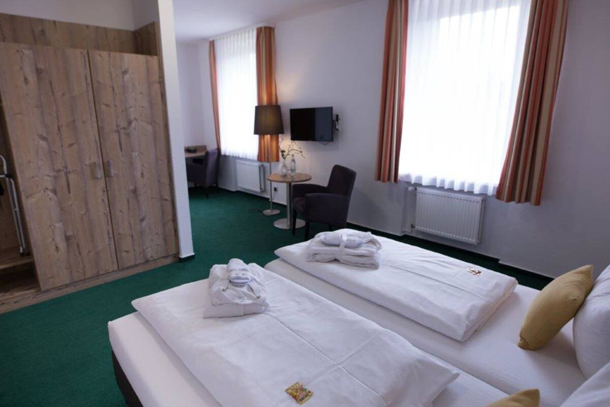 Een hotelkamer met twee bedden, een bureau, een stoel, een televisie en een houten garderobe.