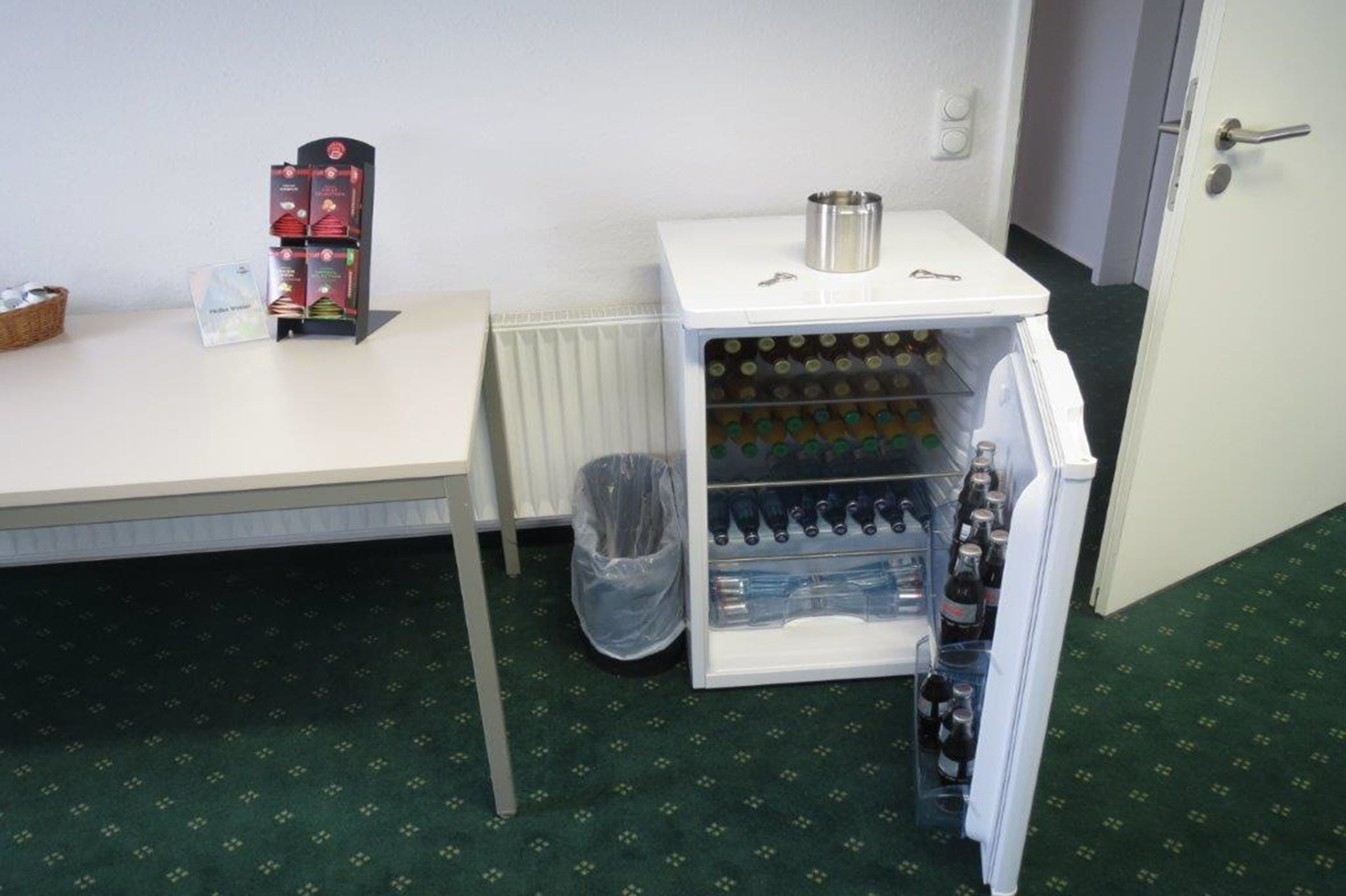 A compact hotel room with a small table, a minibar, and a door.