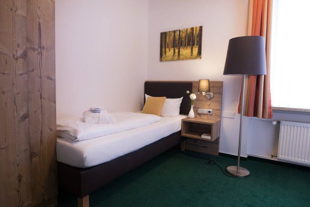 Een hotelkamer met een bed, nachtkastje, lamp en een schilderij aan de muur.