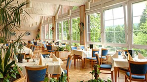 A spacious indoor dining area with large windows, wooden tables, and blue chairs. - BSW - Erlebnishotel Festenburg (Clausthal-Zellerfeld)