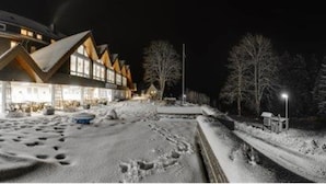 A snow-covered outdoor area with a building featuring a large, illuminated entrance and a sloped roof. - BSW - Erlebnishotel Festenburg (Clausthal-Zellerfeld)