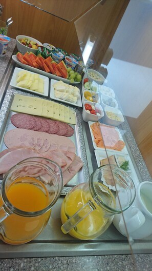 Una mesa de buffet con una gran variedad de alimentos, incluyendo carnes, quesos, frutas y bebidas.