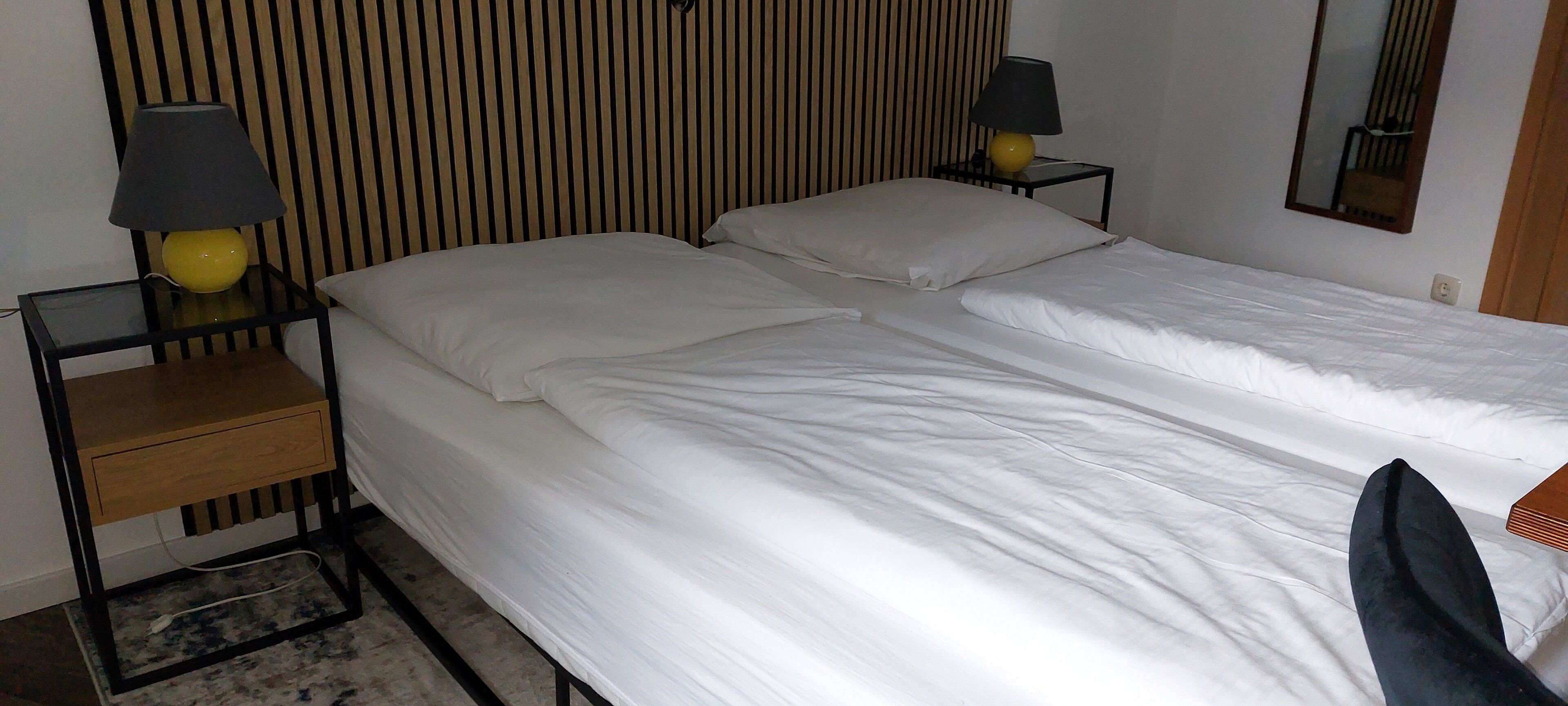 A neatly made bed with white linens, two bedside tables with lamps, a wooden headboard, and a mirror on the wall.
