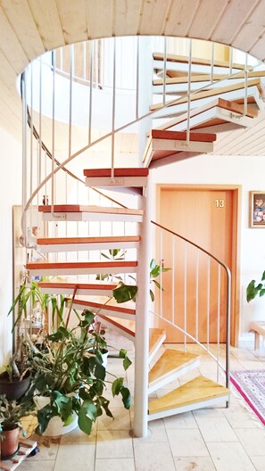 Un escalier en colimaçon avec des rampes blanches et des marches en bois, menant à une porte portant le numéro 13.