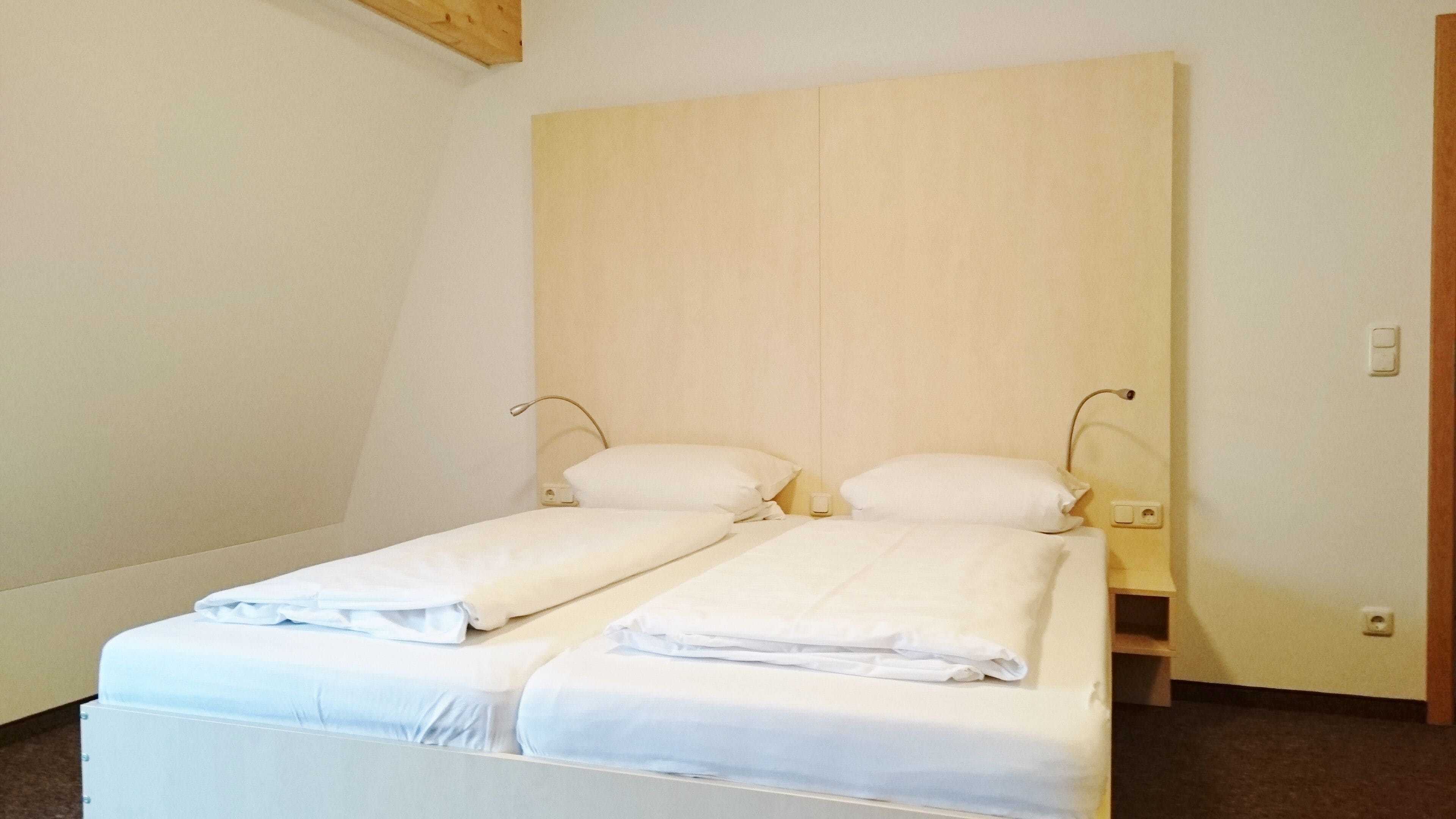 A single bed with a wooden headboard, two bedside tables, and a wall socket.