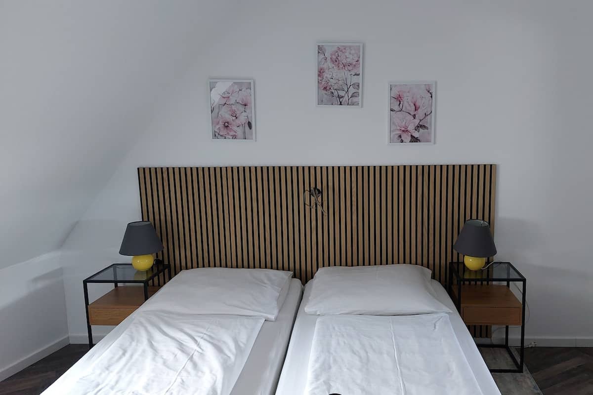 Ein Doppelbett mit gestreifter Kopfteil, zwei Nachttische mit Lampen und drei gerahmte Blumenbilder an der Wand.