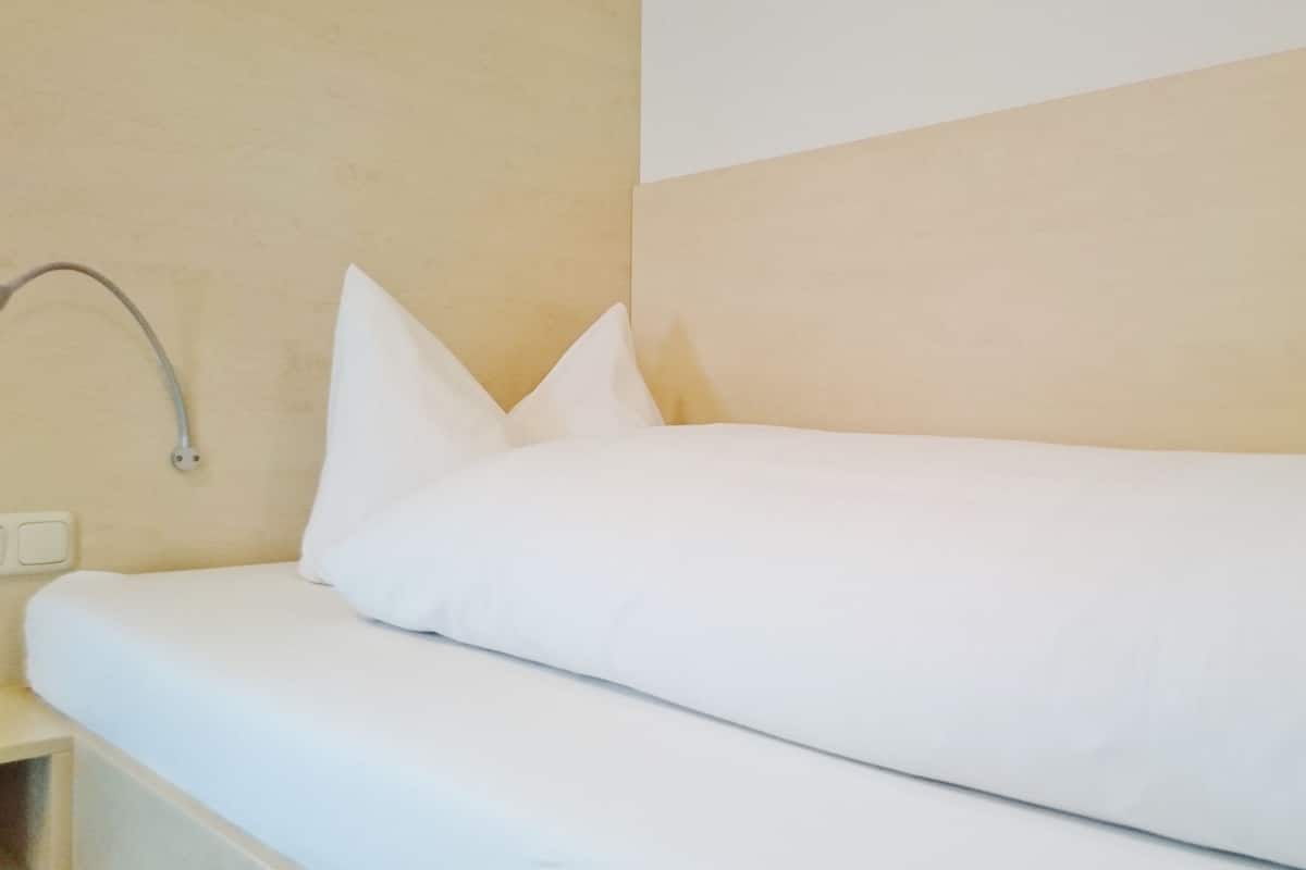 Ein Einzelbett mit weißer Bettwäsche in einem Zimmer mit beige gefärbten Wänden und einer weißen Decke.