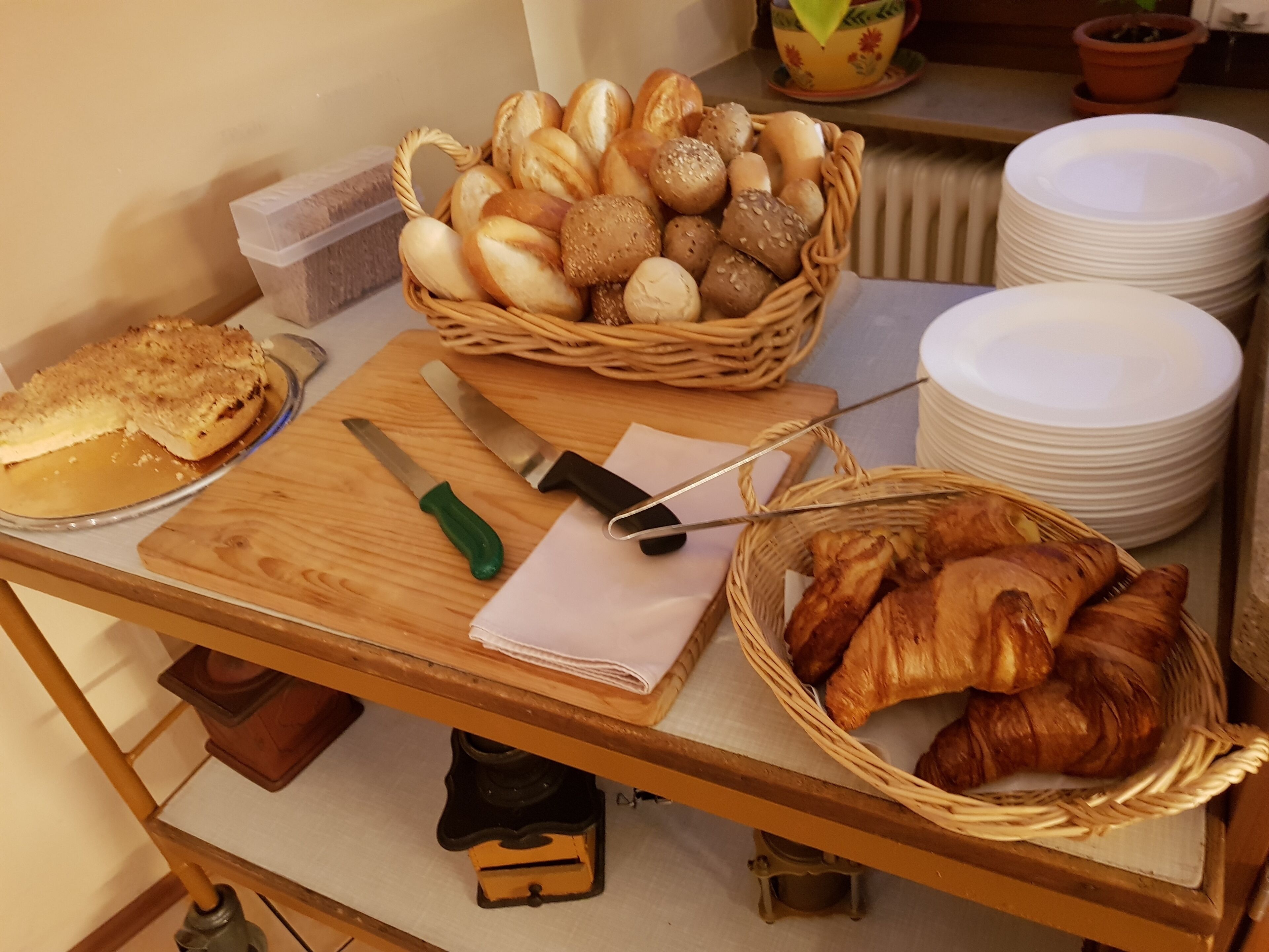 A breakfast buffet with various breads, croissants, and a knife on a wooden table.