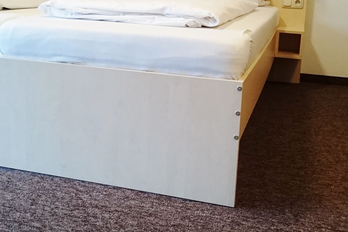 Ein Doppelbett mit weißer Bettwäsche, ein Holz-Kopfteil und ein Nachttisch mit Lampe.