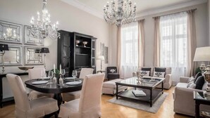 A spacious living room with a dining area, featuring a chandelier, a black cabinet, and a sofa set. - Palacina Berlin Apartments (Berlin)