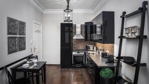 A modern kitchen with black cabinetry, a dining area with a black table and chairs, and a decorative green plant. - Palacina Berlin Apartments (Berlin)
