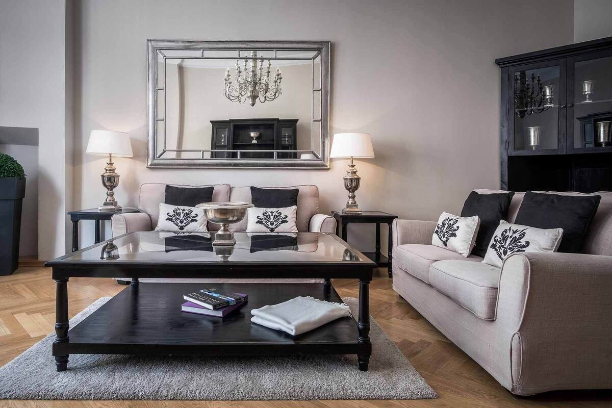 Ein Wohnzimmer mit einem Glastisch, zwei Sofas, einem großen Spiegel und einer Pendelleuchte.