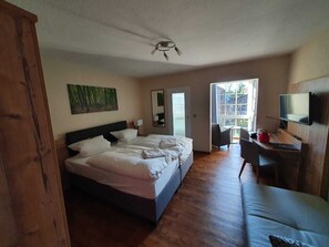 Un dormitorio con una cama grande, un escritorio con silla, un televisor y una ventana con vista a árboles.