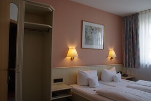 A hotel room with a bed, two bedside lamps, a nightstand, a framed picture on the wall, and a window with curtains. - Zum Treuen Bartel (Markgröningen)