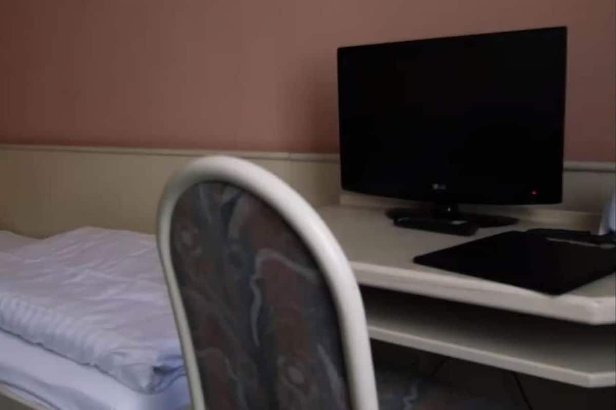 Una cama individual con un almohadón blanco y un televisor de pantalla plana sobre un escritorio.