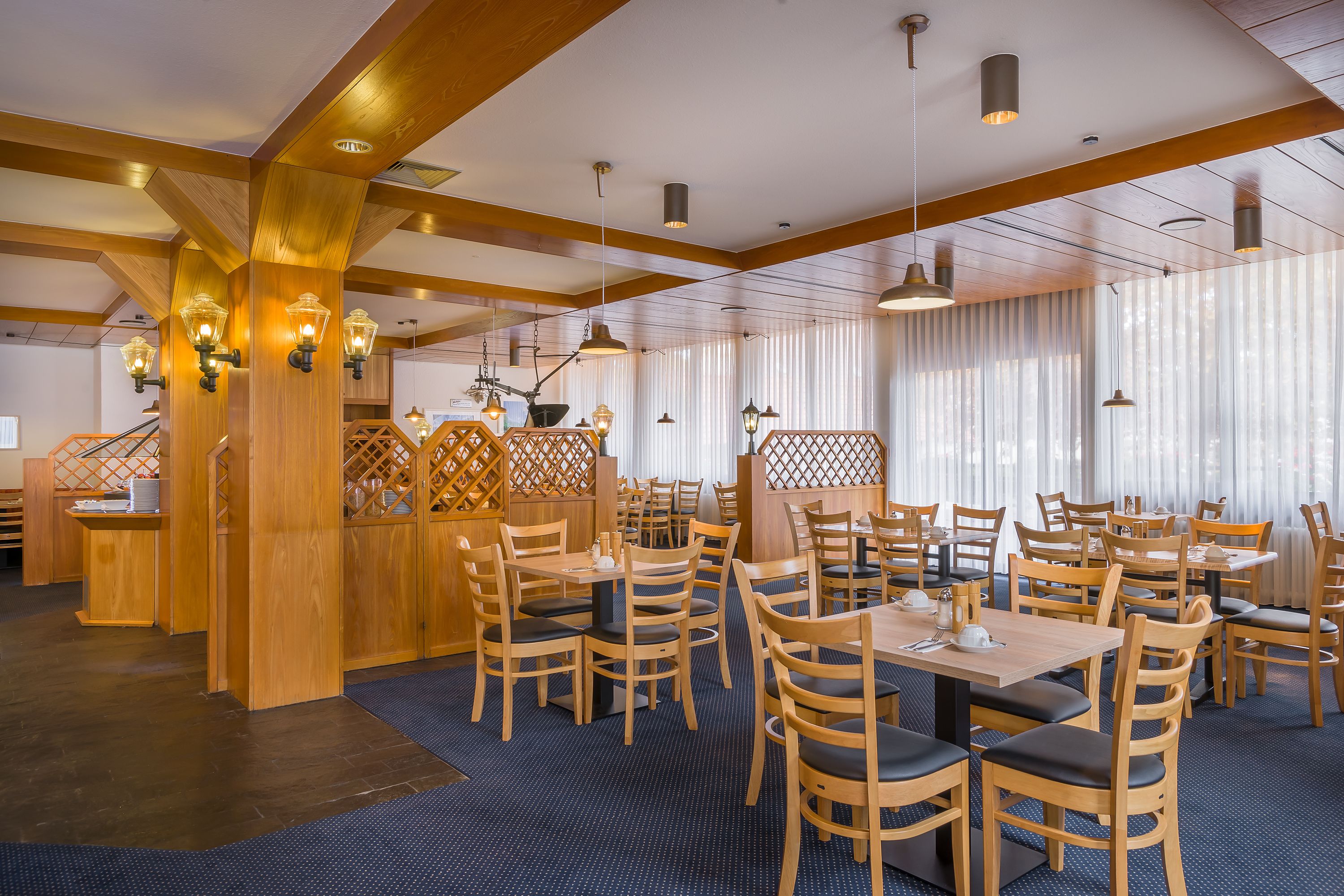 A restaurant with wooden furniture, pendant lighting, and a blue carpeted floor.