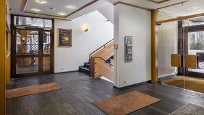A modern hotel lobby with a wooden staircase, a reception desk, and a glass door leading outside. - Hotel Strohgäu (Korntal-Munchigan)