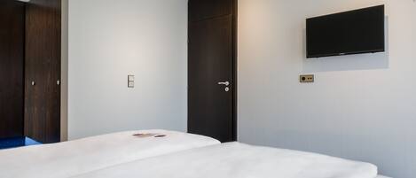 Una habitación de hotel con cama, armario, puerta y televisor montado.
