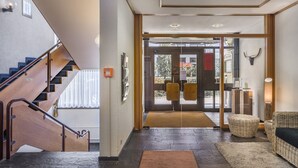 A modern hotel lobby with a wooden staircase, a reception desk, and a view of the outside. - Hotel Strohgäu (Korntal-Munchigan)