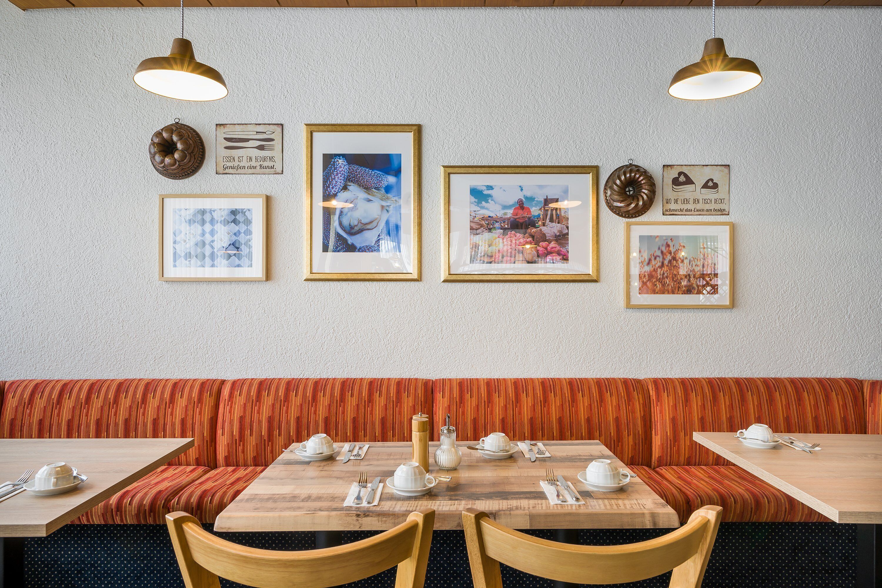 Ein Restaurant mit Holztischen und -bänken, gerahmten Bildern an der Wand und hängenden Lampen.