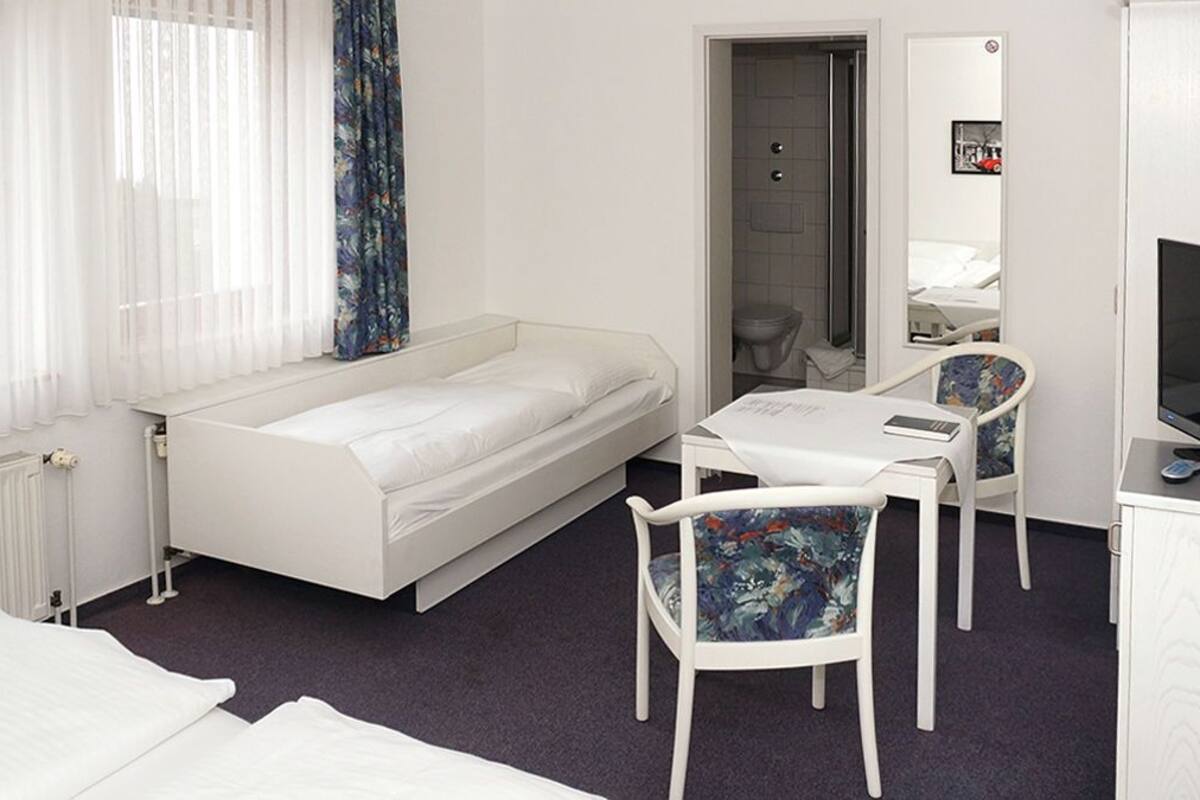A hotel room with a bed, a desk with a chair, a TV, and a mirror.