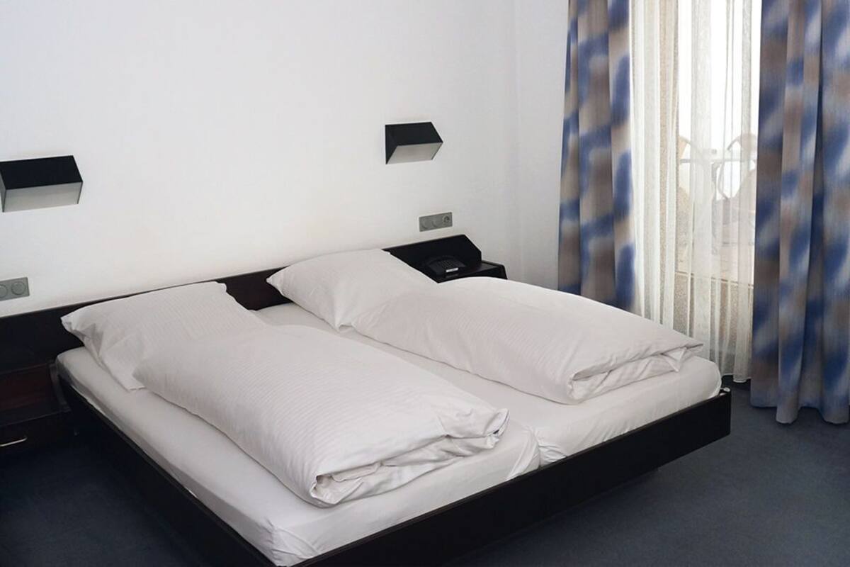 A hotel room with a single bed, a bedside table, a nightstand, and a window with curtains.