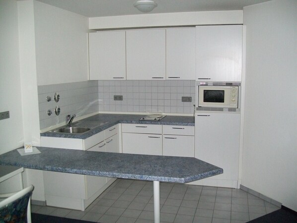 A compact kitchen with white cabinets, a built-in microwave, a sink, and a granite countertop. - Hotel Gasthof Traube (Kernen)