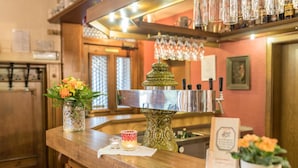 A bar area with a polished metal bar counter, a decorative metal pitcher, and a vase with flowers. - Hotel Zum Specht (Hoesbach)