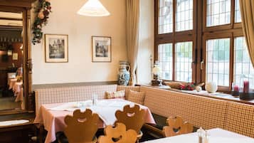 Un comedor acogedor con asientos tipo camarote a cuadros, sillas de madera y un amplio ventanal con cortinas.