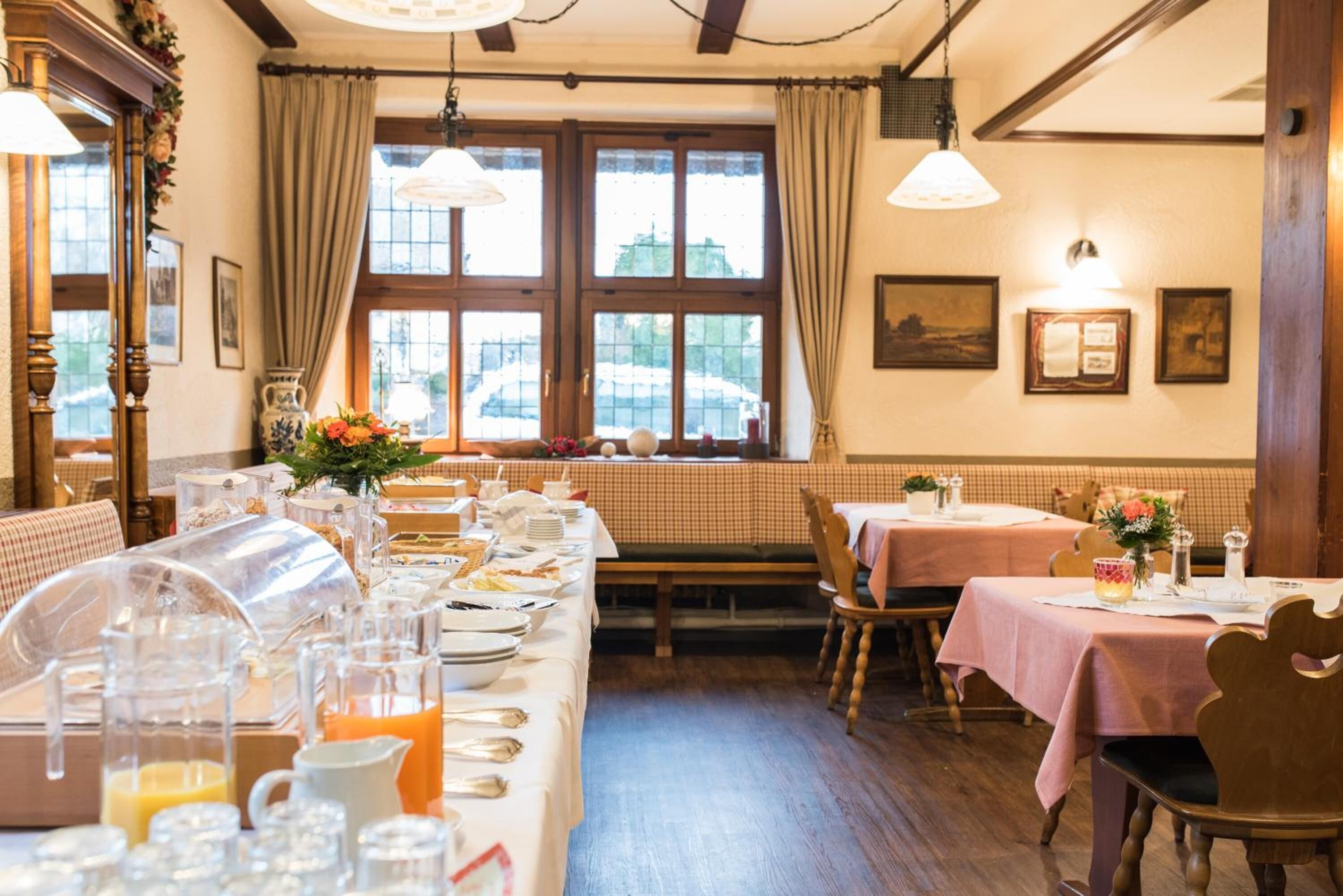 A dining area with a long table set for breakfast, wooden chairs, and a window with curtains.