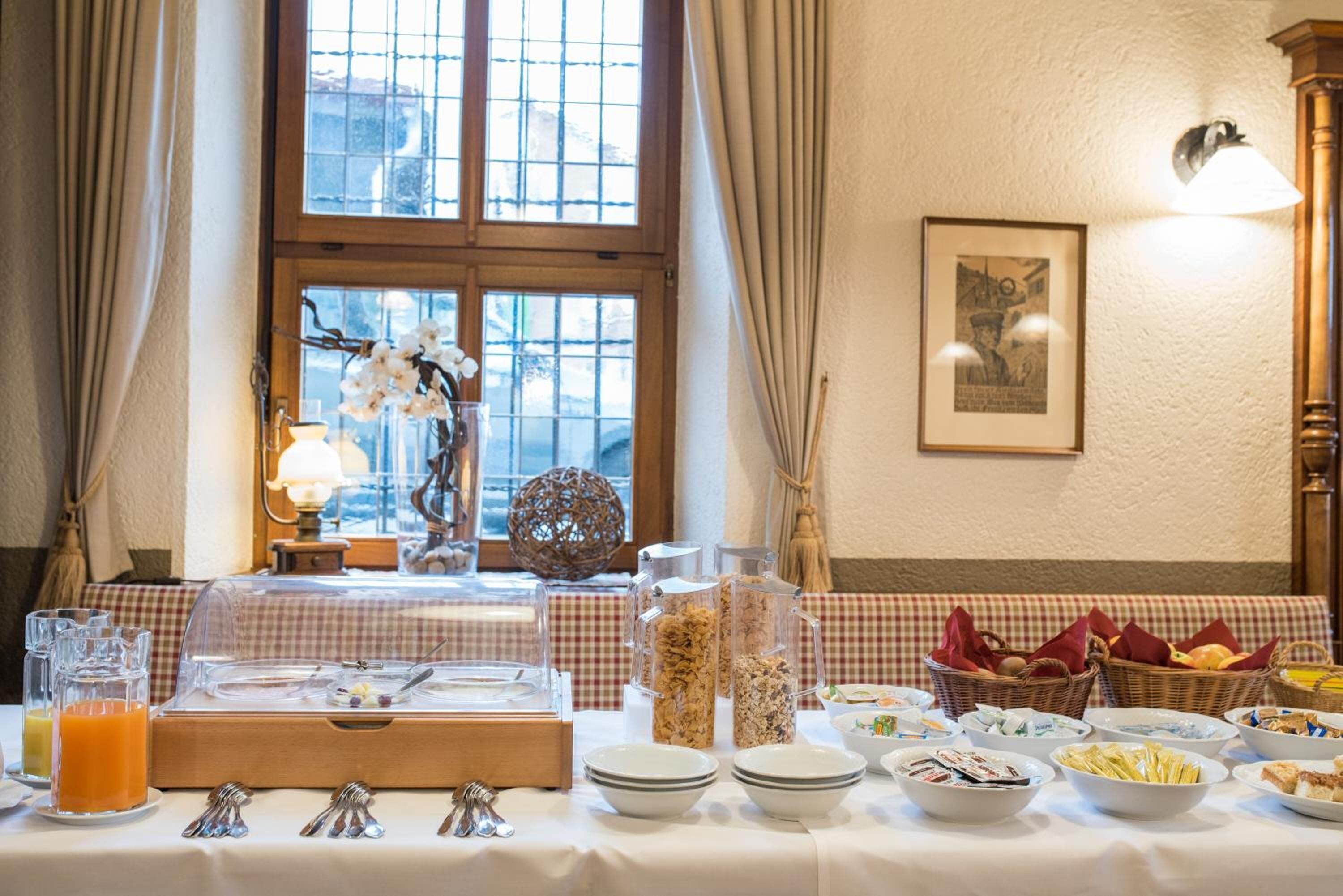 A breakfast buffet setup with a variety of food items and beverages, a checkered tablecloth, and a window with curtains.