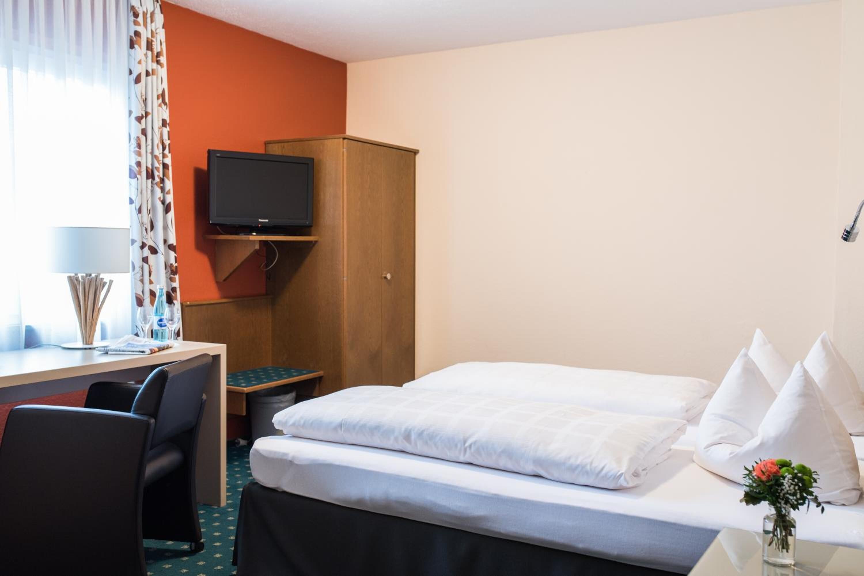 Habitación de hotel con cama, escritorio, silla, televisor y armario.